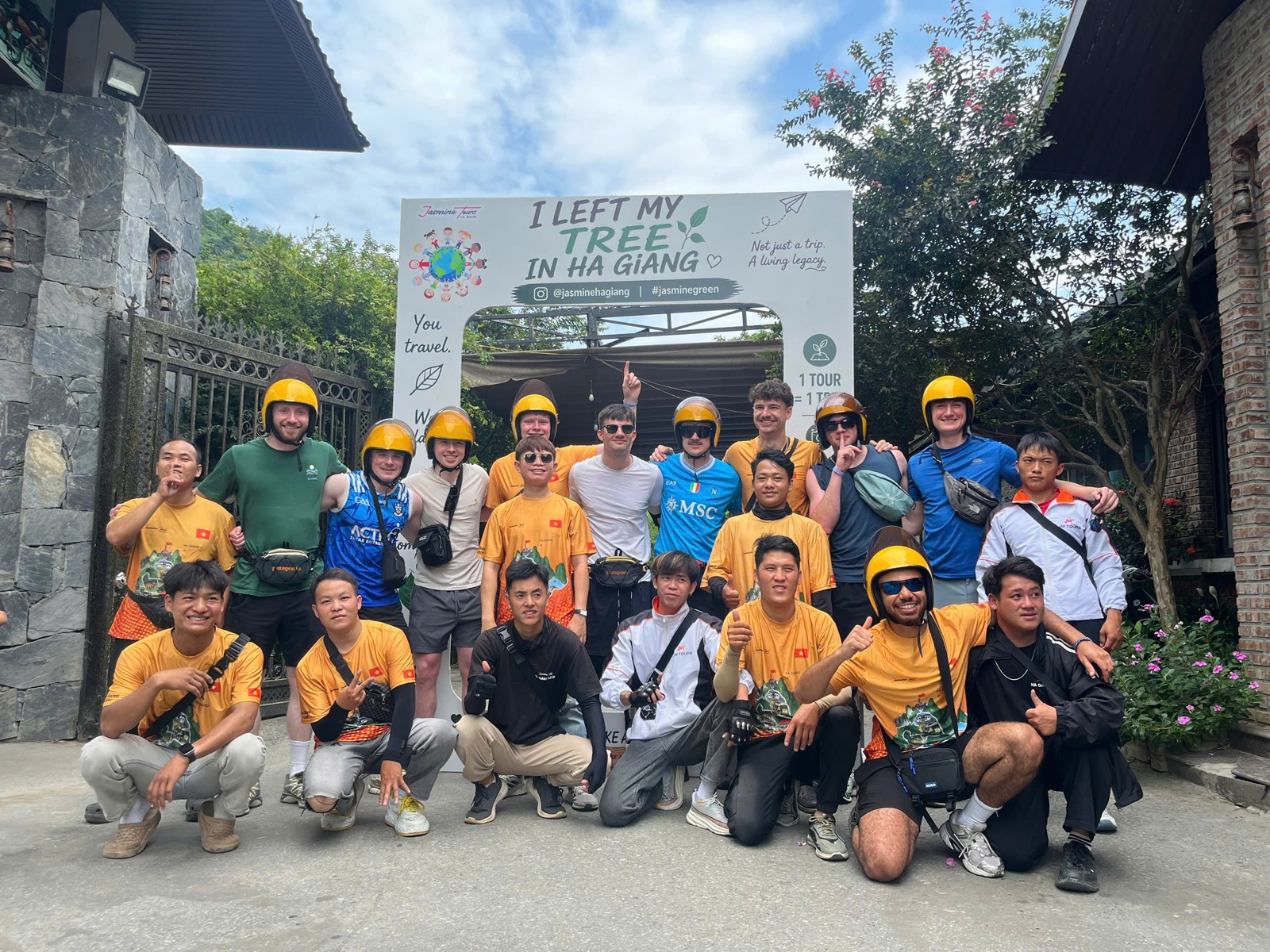 Local Ha Giang team in orange shirts standing with international travellers under an I Left My Tree In Ha Giang sign