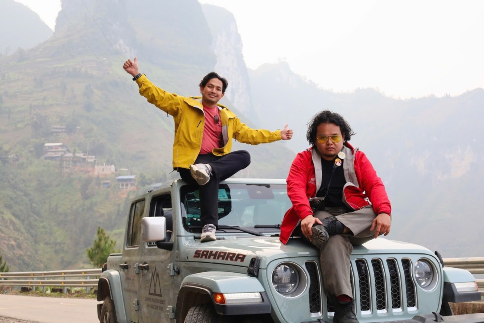 Two local Ha Giang drivers with a Jeep on a mountain road below limestone karst peaks on the Ha Giang Loop