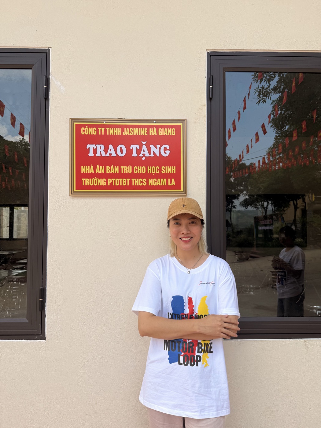 Thuy Bui in a Ha Giang motorbike loop shirt beside a plaque marking a school canteen donated to a local boarding secondary school in Ngam La, Ha Giang