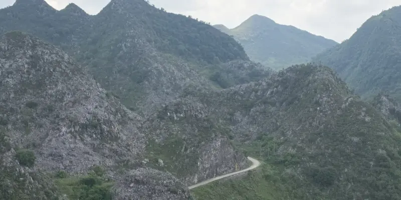 A single-lane road cut into grey karst ridges on the Ha Giang Loop, curving out of sight between two peaks