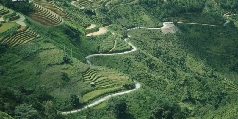 A narrow paved road winding down through terraced hillsides and green mountains on the Ha Giang Loop