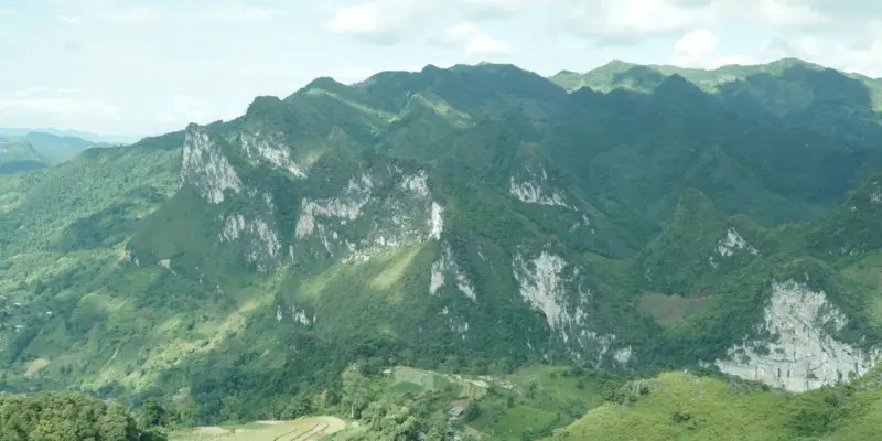 Grey limestone karst ridges above a cultivated green valley with scattered buildings in Ha Giang, northern Vietnam