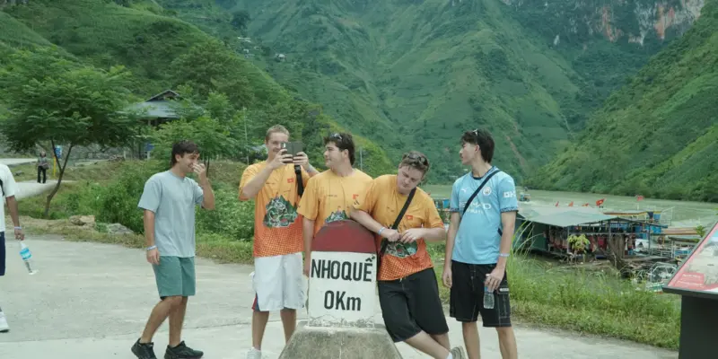A group of travellers standing at the Nho Que 0km marker in Ha Giang, green mountains behind them