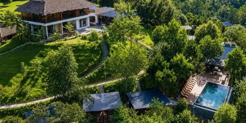 Jashill Homestay seen from the air, rooms strung along the hillside above Du Gia's rice terraces, August 2026