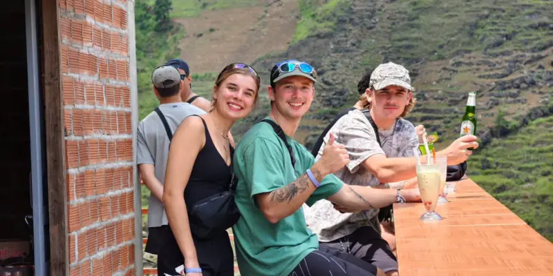 Travellers sitting with drinks at a roadside bar counter in Ha Giang, green hills behind them