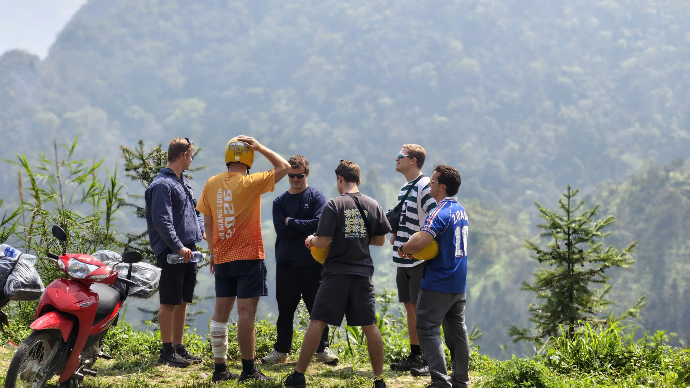 Travellers standing beside parked motorbikes on a hazy mountain road in Ha Giang, April 2026