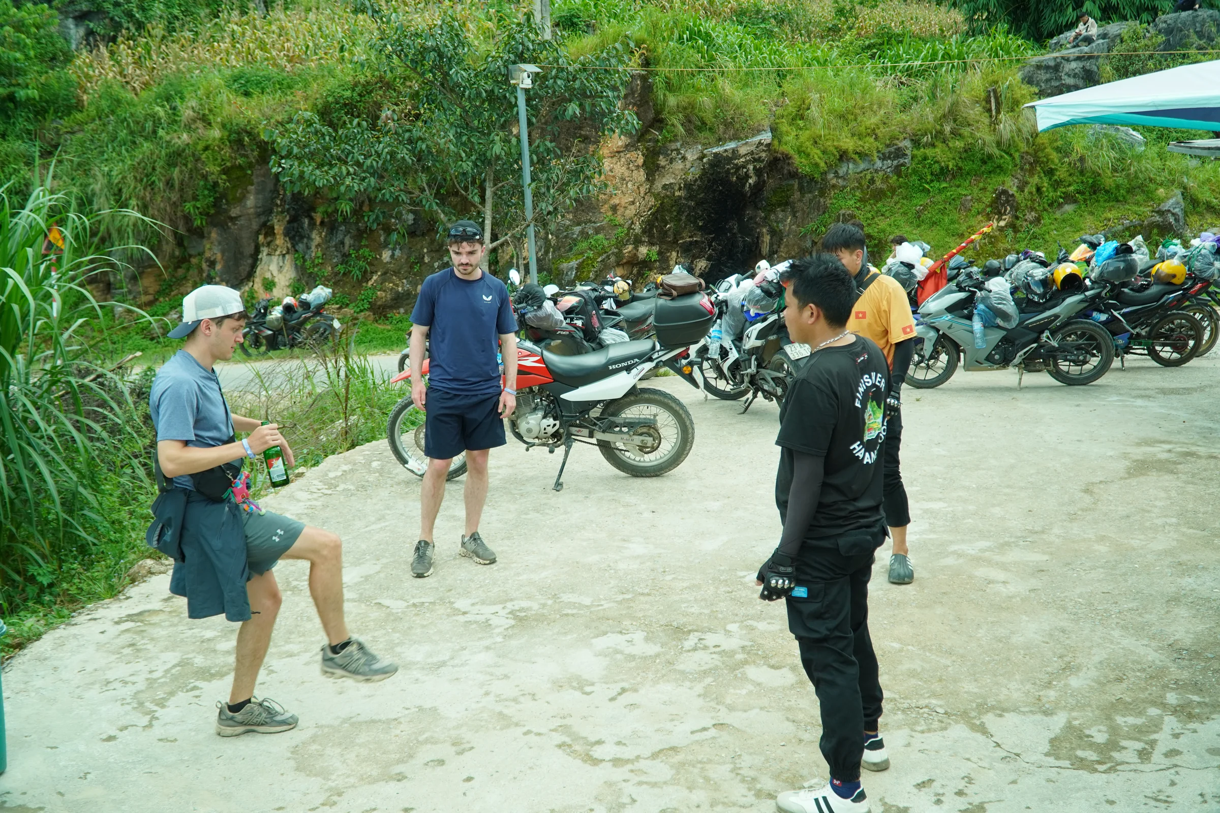 A line of motorbikes parked at a roadside stop on the Ha Giang Loop while travellers stand and talk beside them