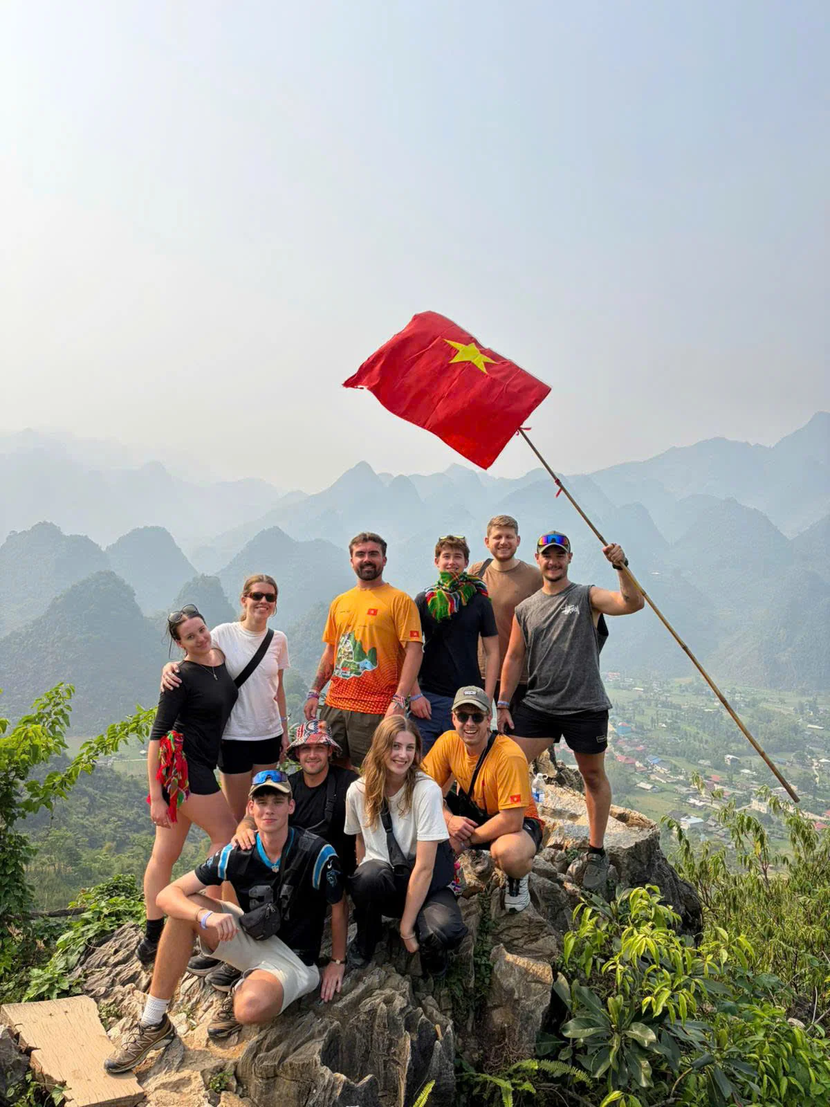 Travellers standing on a rocky outcrop beside a mountain road in Ha Giang with karst peaks behind, May 2026