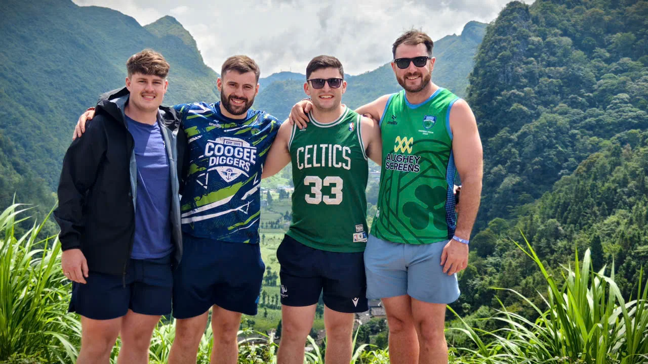 Three travellers standing on a mountain road in Ha Giang with karst peaks behind, June 2026