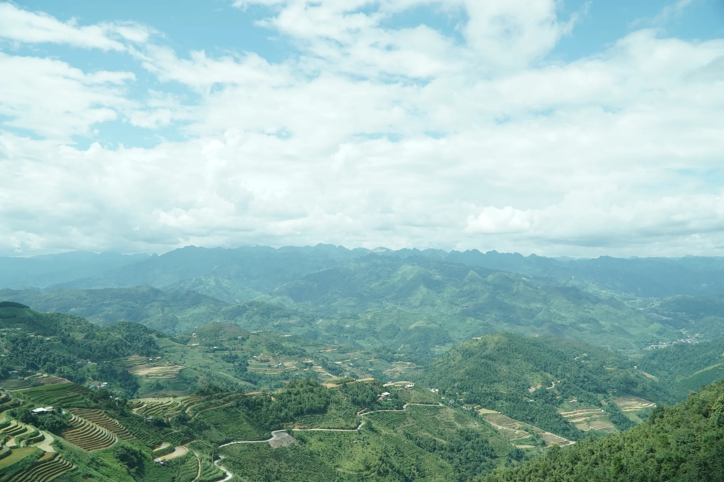 Green terraced hillsides and a road winding through northern Vietnam under broken cloud