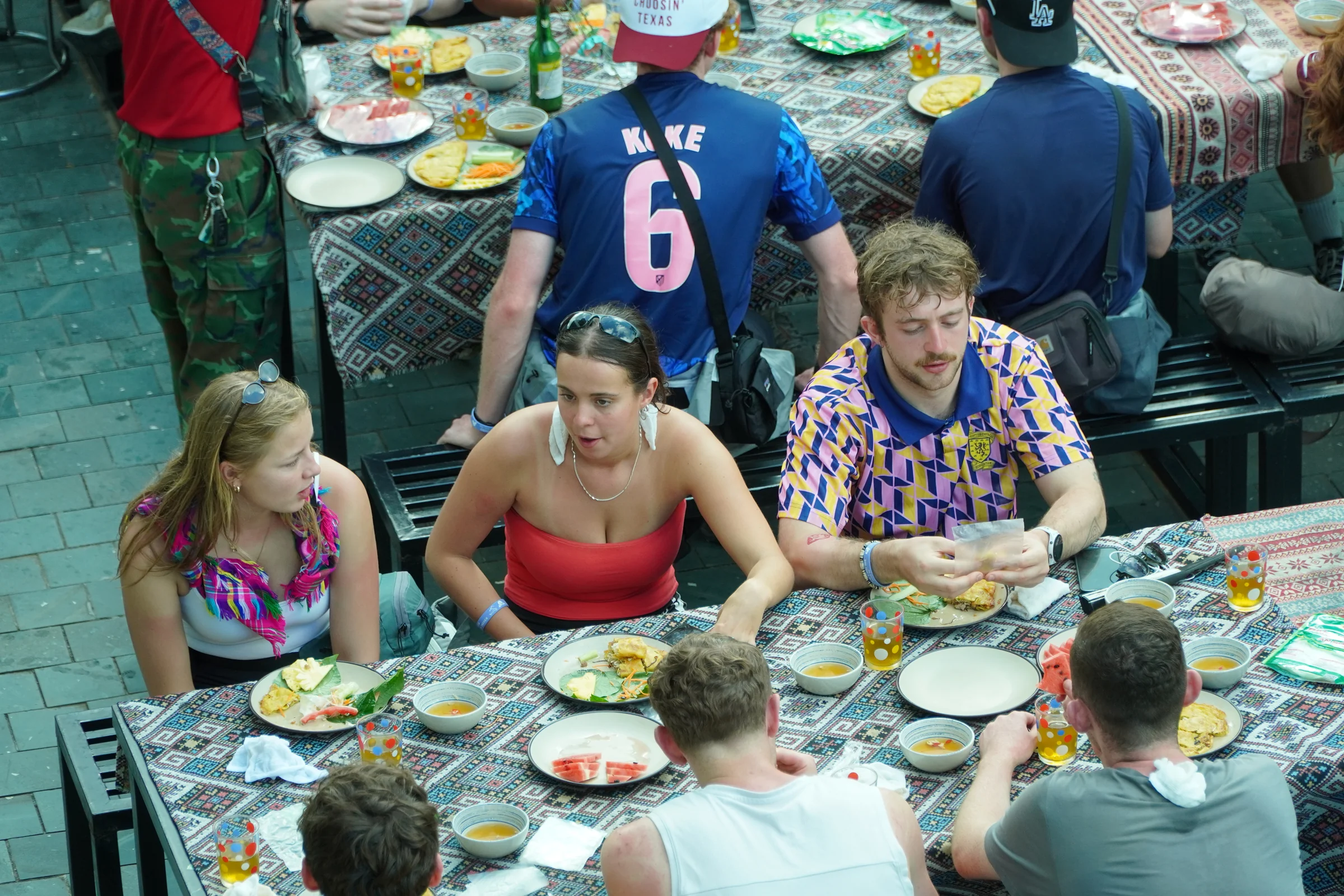 Travellers eating a shared meal at long tables set with rice and small dishes at a stop on the Ha Giang Loop