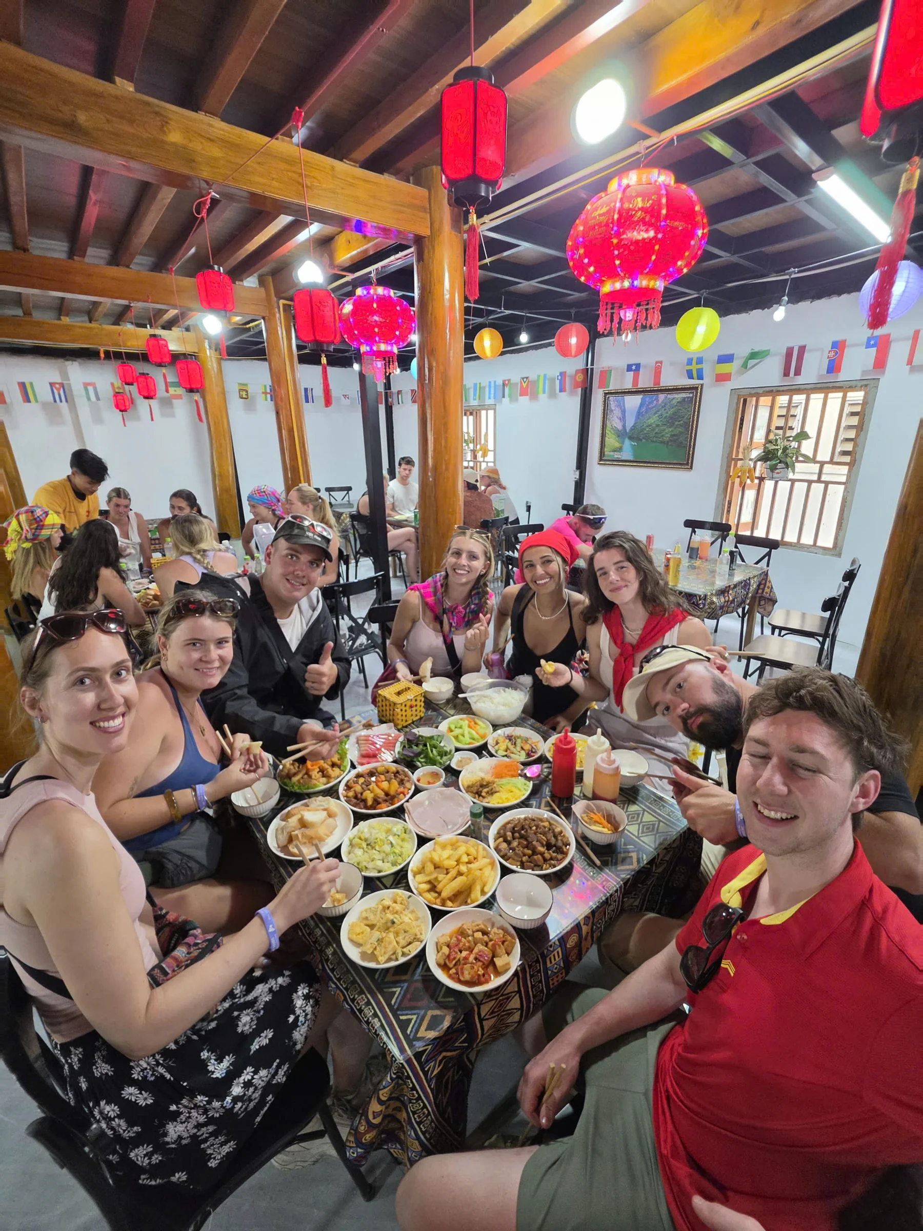 A long table of travellers sharing bowls of food under red lanterns at a Ha Giang homestay