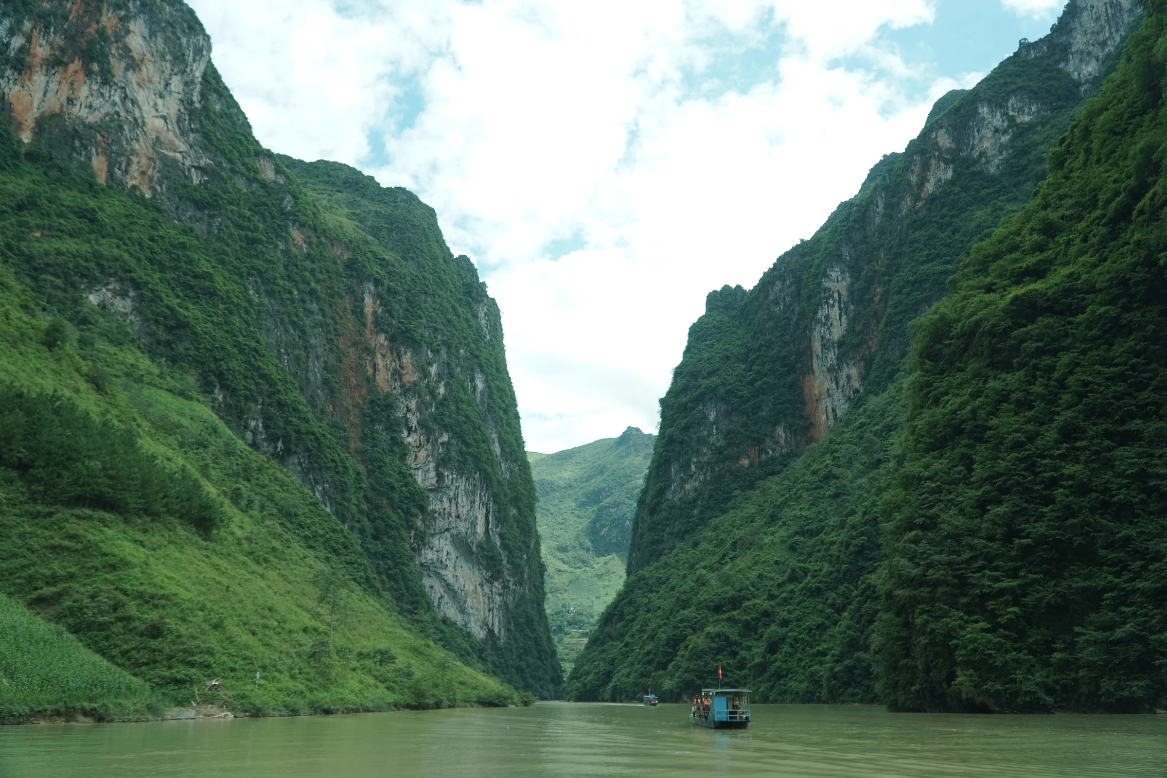 The Nho Que river running between near-vertical limestone walls in the Tu San canyon, Ha Giang, a small boat visible far downstream
