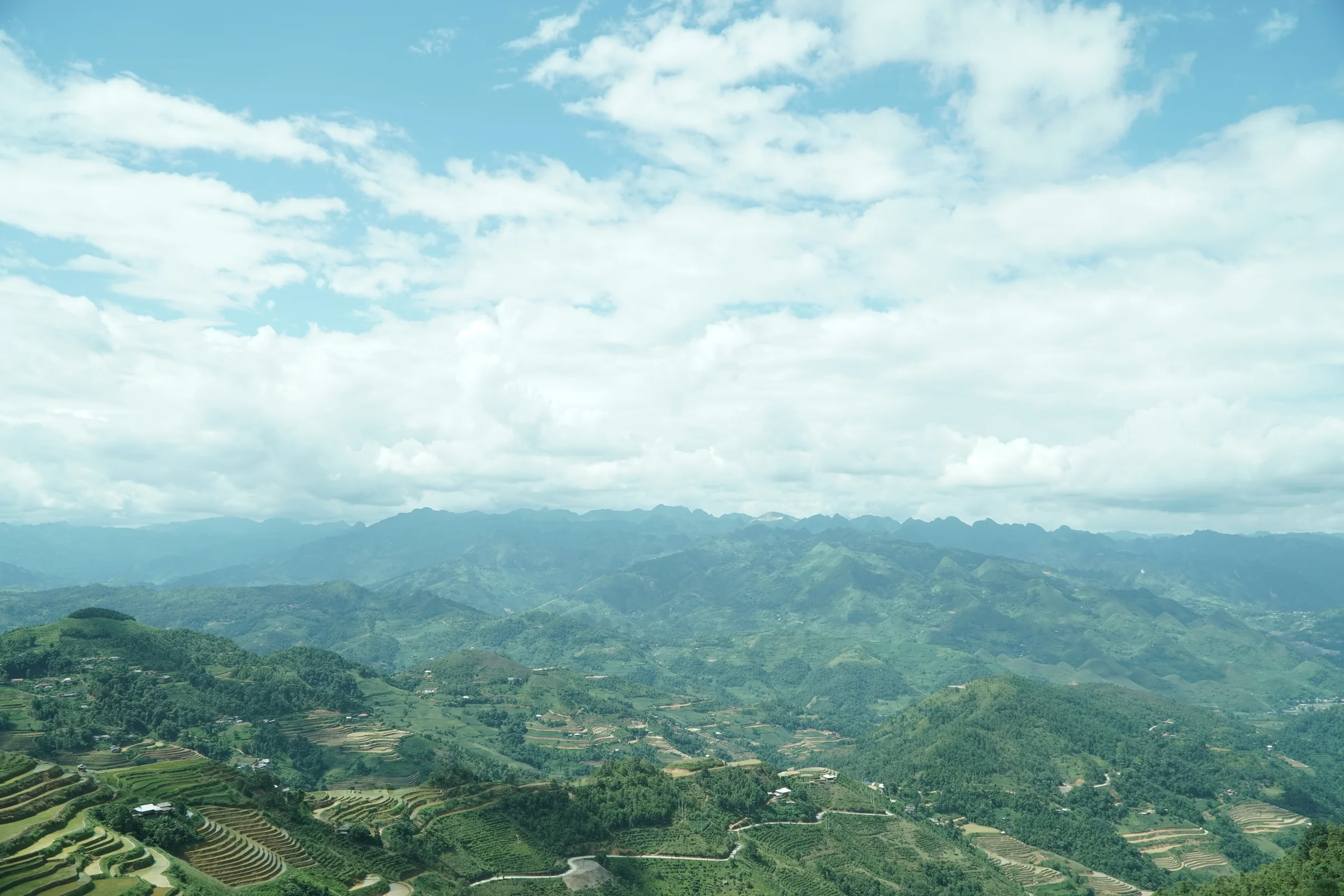 Terraced hillsides and a winding road under a clear sky in northern Vietnam, ridges fading into the distance