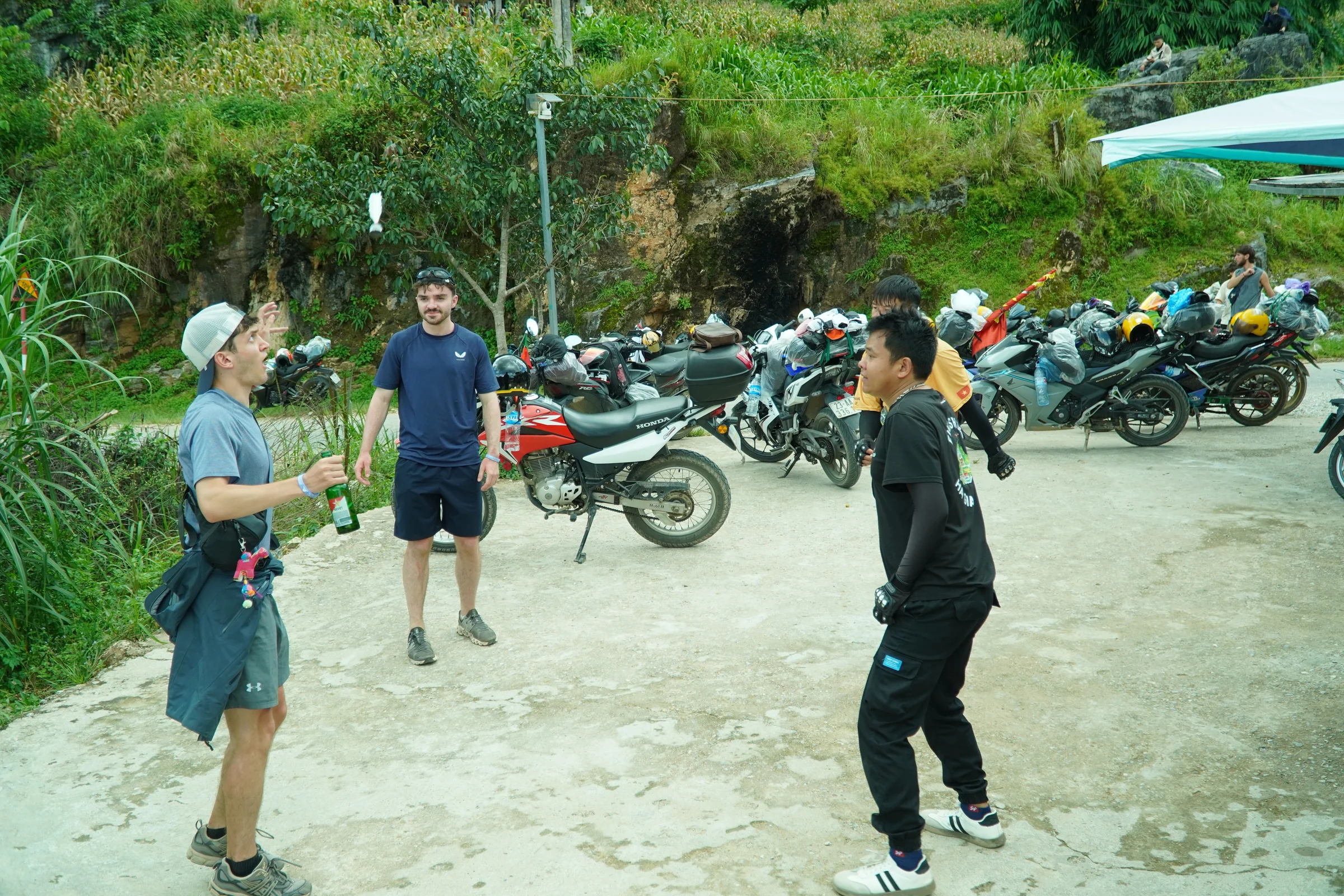 A row of rented motorbikes parked on gravel at a roadside stop on the Ha Giang Loop, riders standing among them