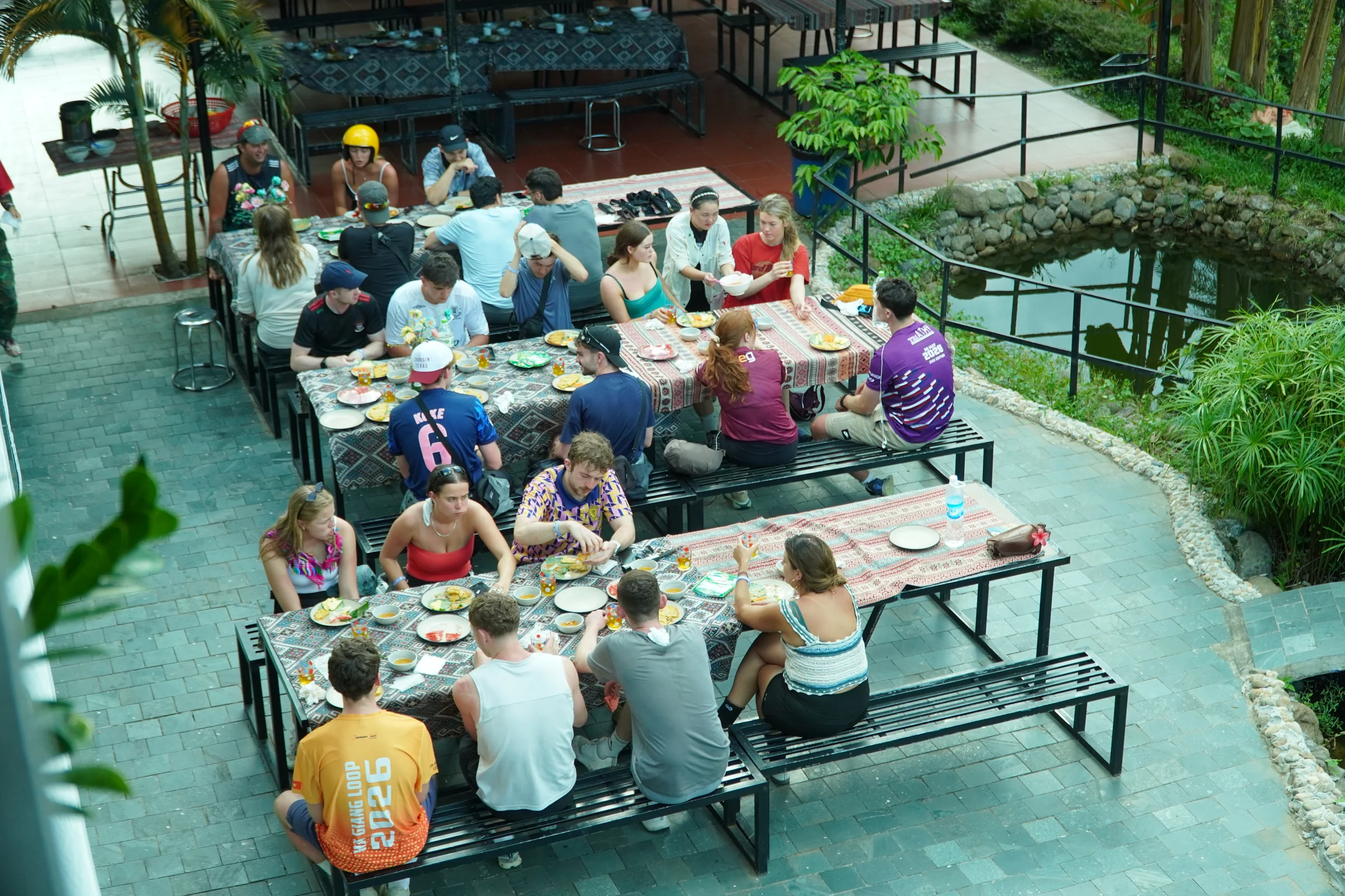 A long table of riders and guests eating together at a roadside stop on the Ha Giang Loop, seen from above