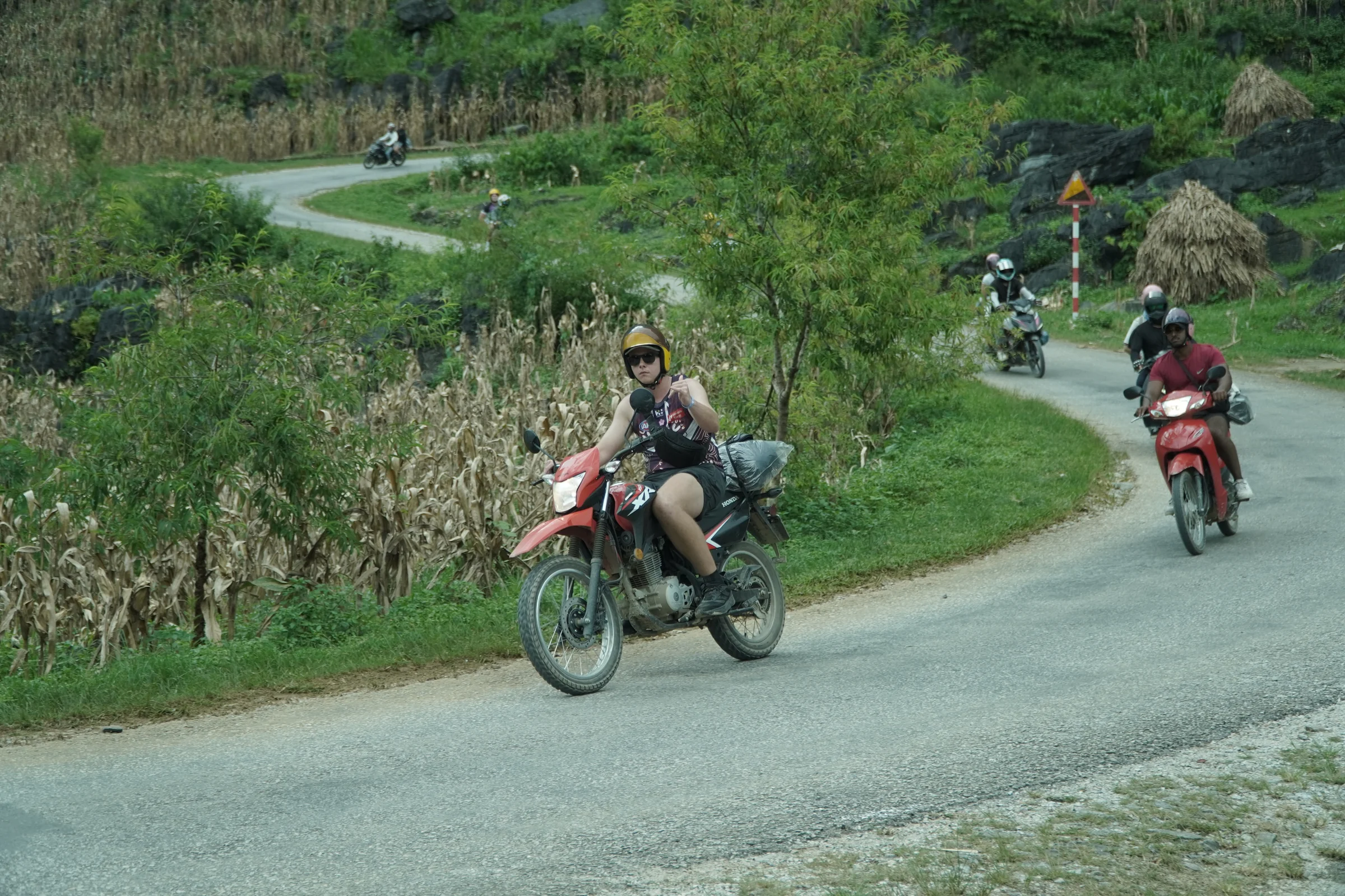 Motorbikes strung out along a wide bend of a Ha Giang Loop road, one rider leading and more following behind