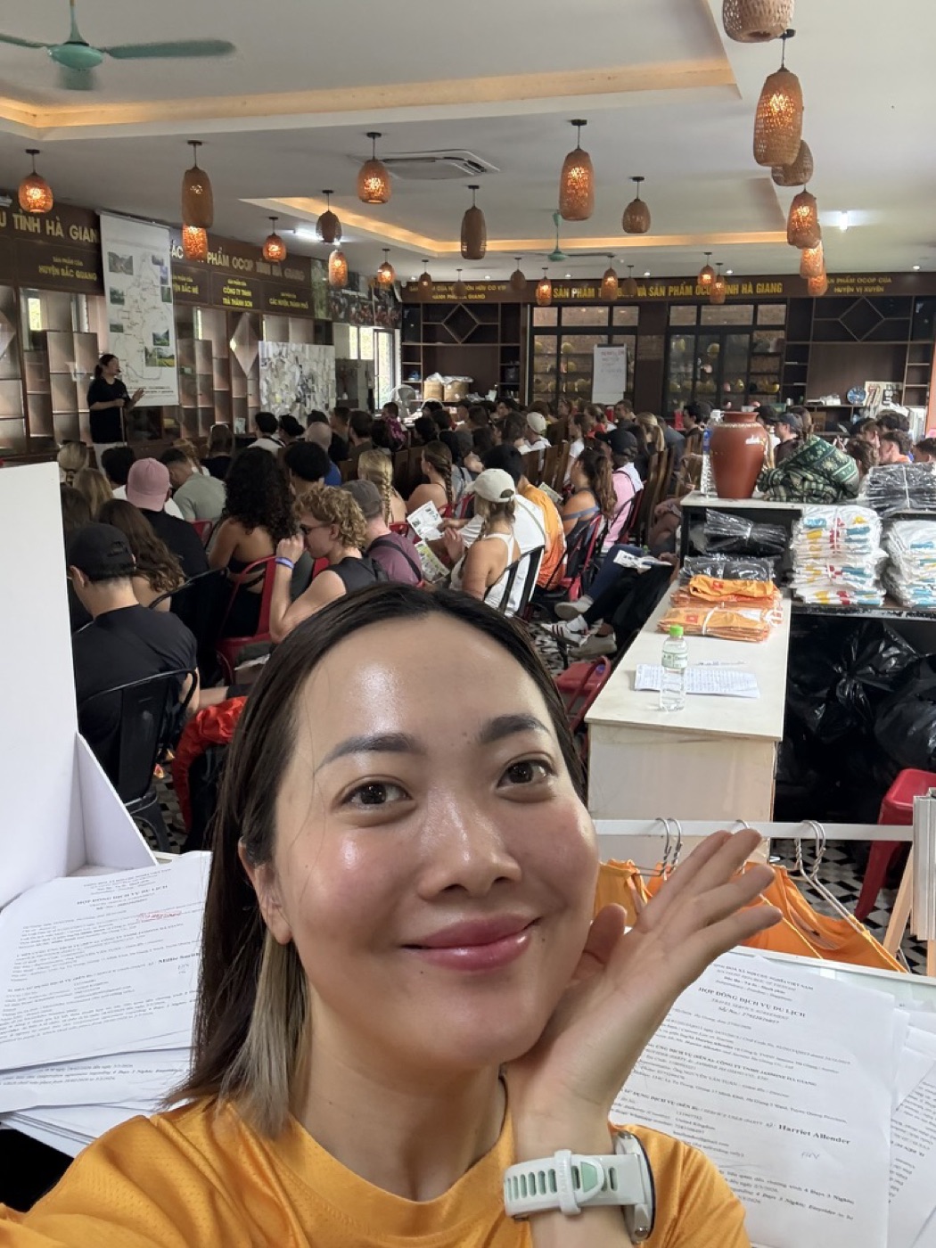 Thuy Bui at work in Ha Giang, holding trip paperwork in a hall full of international travellers